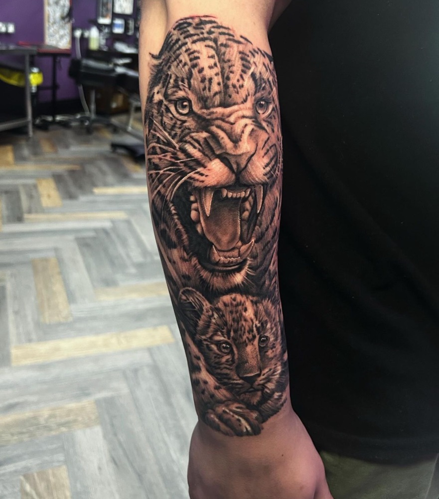 Black and grey realism tattoo of a roaring leopard and cub on a forearm